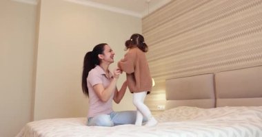 Gülen anne ve küçük kızı sabah yatak odasında yatağa atlıyorlar, özgürlük ve mutluluk.