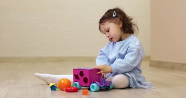 Küçük kız yerde şekil ayırıcı oyuncakla oynuyor, evde eğitim amaçlı oyun zamanı. Bilişsel gelişim aktivitesi