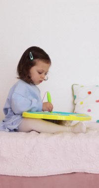 Küçük çocuk yatakta manyetik silinebilen tahtaya resim çiziyor.