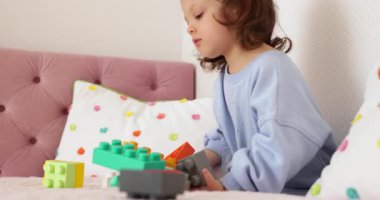 Küçük kız yatakta inşaatçılık oynuyor. Çocuk oyuncak tuğlalarla inşa ediyor. yapıcı küpleri