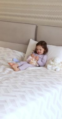 Bebek bebek yatakta oyuncak bebekle oynar, bebek saçlarını tarar.