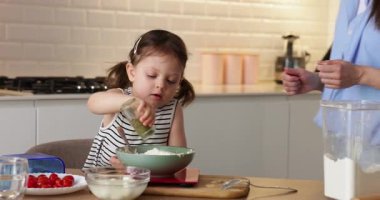 Şirin kız yemek yapmayı öğreniyor, yeni yürümeye başlayan kız annesine modern mutfakta pasta hazırlamakta yardım ediyor.