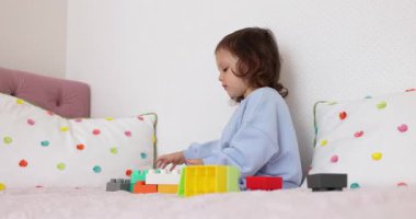 Küçük kız yatakta inşaatçılık oynuyor. Çocuk oyuncak tuğlalarla inşa ediyor. yapıcı küpleri