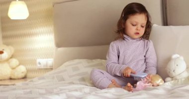 Bebek bebek yatakta oyuncak bebekle oynar, bebek saçlarını tarar.