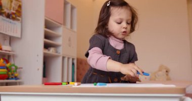 Evdeki beyaz kağıda kurşun kalemle resim çizen küçük şirin bir kız çocuğu. Yaratıcı aktivite.