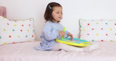 Küçük çocuk yatakta manyetik silinebilen tahtaya resim çiziyor.