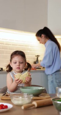 Küçük kız mutfakta hamur yoğuruyor, kız çocuğu annesine yemek pişirmesinde yardım ediyor.