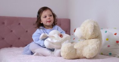 Küçük tatlı kız evde yatakta oyuncak ayıyla oynuyor..