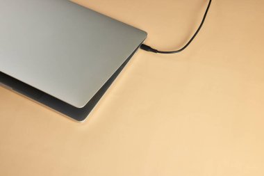 Bej arka planda dizüstü bilgisayara bağlı kablo, yakın plan. Pil dizüstü bilgisayarı yükleniyor, üst görünüm