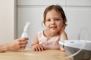 Anne, küçük tatlı kızına evde nebulizatörle ilaç solumasında yardım ediyor.