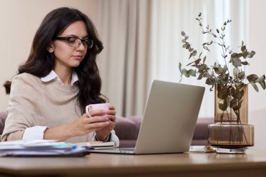 Evde çalışırken dizüstü bilgisayar kullanan gömlekli güzel bir kadın.