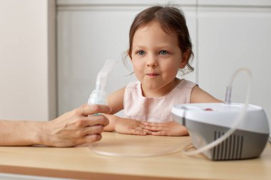 Küçük tatlı kız nebulizörü evde tutan annesinin yardımıyla solunum yapıyor.