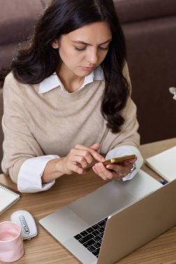 Kadının portresi akıllı telefon tutuyor. Ev ofisinde dizüstü bilgisayar kullanıyor.