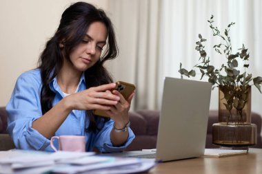 Mavi gömlekli kadın portresi ev ofisinde dizüstü bilgisayar kullanıyor.