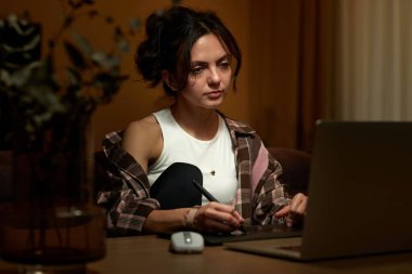 Güzel grafik tasarımcı kadın ev ofisinde dijital tablet ve laptop kullanarak çalışıyor.