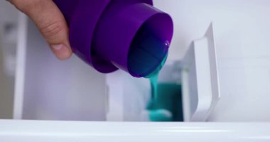 Kadın eli çamaşır makinesinin kompartımanına sıvı deterjan döküyor.