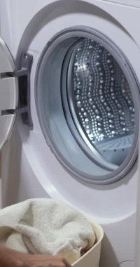 Evde çamaşır yıkayan sepetli bir kadın, çamaşır makinesinin variline beyaz çamaşır yükleyen bir kadın..