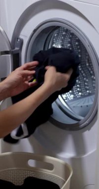 Çamaşır sepetini yıkayan bir kadın, çamaşır makinesinin variline siyah çamaşır yükleyen bir kadın. yakın plan