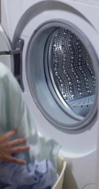 Kadın eli mavi çamaşırları çamaşır makinesinin variline dolduruyor. yakın plan