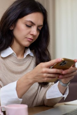 Kadının portresi akıllı telefon tutuyor. Ev ofisinde dizüstü bilgisayar kullanıyor.