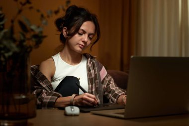 Güzel grafik tasarımcı kadın ev ofisinde dijital tablet ve laptop kullanarak çalışıyor.