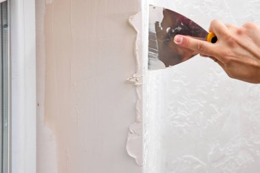 Elinde spatulası olan beyaz alçı adam pencere açılışına macun sürüyor.