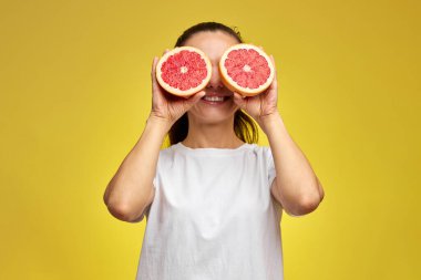 Beyaz kadın, sarı arka planda greyfurtla gözlerini kapatıyor.
