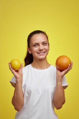 Sarı arka planda taze limon ve greyfurt tutan mutlu kadın, sağlıklı beslenme.
