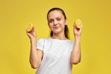 Gülümseyen esmer kadın sarı arka planda taze limon dilimi tutuyor, vitamin meyve diyeti.
