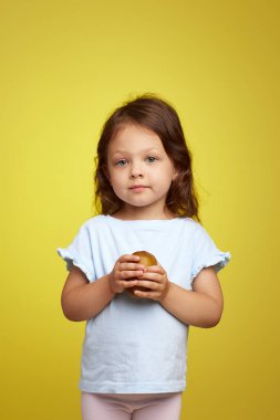 Sarı arka planda kivi meyvesi tutan beyaz bir kız çocuğu.