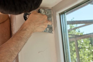 Elinde spatulası olan beyaz alçı adam pencere açılışına macun sürüyor.