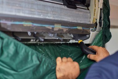 Temizlik servisinden erkek işçi, klimayı su püskürterek temizliyor, yakın plan.