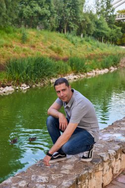 Parktaki bir kanalın kıyısında oturan çekici genç bir adam..