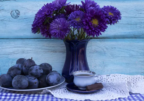 Blue plums, a bouquet of blue asters and a cup of coffee with candy.