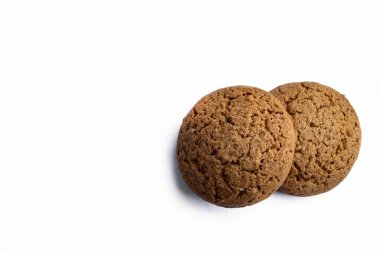 Temiz beyaz arka planda dinlenen iki yuvarlak yulaflı kurabiye altın dokularını ve ev yapımı cazibelerini ön plana çıkarıyor. Fırın promosyonları, yemek fotoğrafçılığı ya da konforlu, tatlı basitlik için mükemmel.