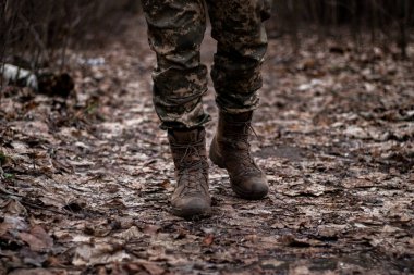 Düşen yapraklarla kaplı ormanda yürüyen bir asker, bacaklarından beline kadar yakalanmış. Güç, odaklanma ve insan ile doğa arasındaki bağlantının bir karışımı..