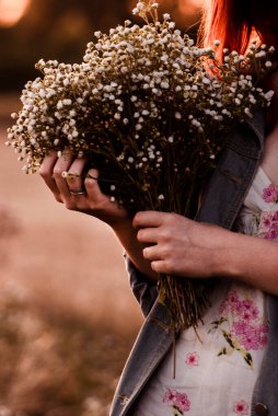 Bir kızın ellerinin bir buket taze papatyayı nazikçe tutuşu. Doğanın basitliğini ve zarafetini yansıtan güzel bir yaz anıydı.