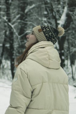 A young woman in warm winter attire standing in a snowy forest, captured from the waist up. A serene and stylish depiction of winter beauty and nature's tranquility clipart