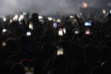 İnsanlar cep telefonlarıyla konser izliyorlar.