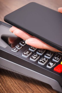 Nakitsiz ödeme yapmak için akıllı telefon ve ödeme terminalini kullanan bir kadın eli. Finans ve bankacılık kavramı