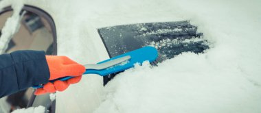 El fırçasıyla araba ve ön camdan kar temizliyor. Ulaşım sırasında kış sorunları