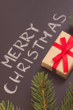 Yazılı Mutlu Noeller, siyah arka planda yeşil ladin dalları ve kurdele ile paketlenmiş hediye. Noel zamanı için dekorasyon