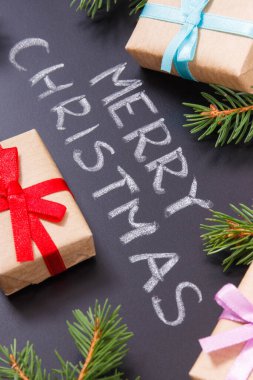 Yazılı Mutlu Noeller, siyah arka planda yeşil ladin dalları ve kurdeleli hediyeler. Noel zamanı için dekorasyon