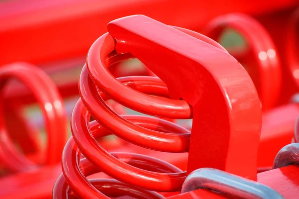 Big and hard red steel spring as part and detail of industrial or agricultural machine. Technology