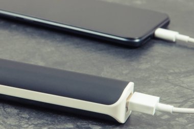Dış güç bankasının bağlı beyaz fişi olan siyah akıllı telefon. Cep telefonu şarj ediliyor