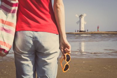 Swinoujscie 'nin batı dalgasında kalp şeklinde güneş gözlüklü bir kadın. Arka planda Windmill Stawa Mlyny karakteristik yön bulma işareti var. Yaz ve tatil zamanı