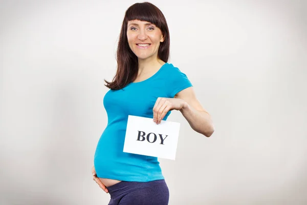 Happy smiling pregnant woman holding white card with inscription boy. Expecting for newborn. Extending family