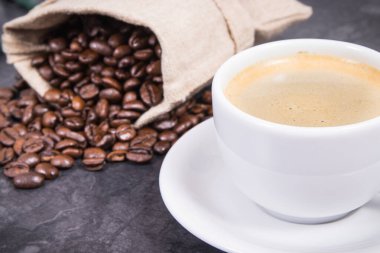 Beyaz fincanda kahve ve kavrulmuş kahve çekirdekleri.