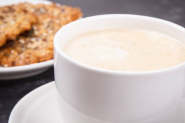 Bir fincan beyaz kahve ve taze ev yapımı yulaf ezmeli kurabiye ve farklı sağlıklı tohumlar. Lezzetli çıtır tatlı.