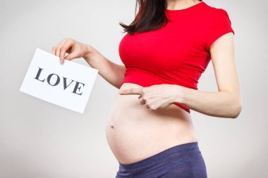 Hamile bir kadının elinde beyaz kart ve yazılı aşk var. Yeni doğan bir bebek bekliyorum. Aileyi genişletmek. Annelik